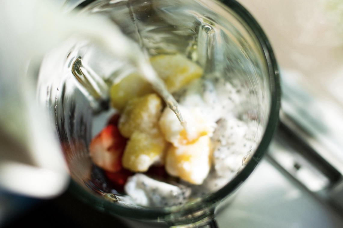 close-up image of a glass blender with fruit making a smoothie preparing to puree