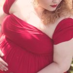 Woman in red dress and lipstick, pregnant, holding stomach.