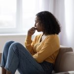 Mental health care. Depressed young black woman suffering from emotional burnout on couch at home. Exhausted African American lady feeling stressed, having psychological problem or nervous breakdown
